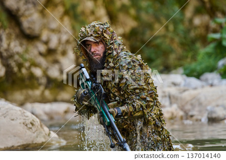 Camouflaged Sniper in Ghillie Suit Wading Through River With Rifle on Tactical Recon Mission Camouflaged Sniper in Ghillie Suit Wading Through River With Rifle on Tactical Recon Mission 137014140
