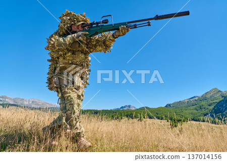 Sniper Soldier In Ghillie Suit With Rifle Patrolling Grassy Mountain Field On Clear Day 137014156