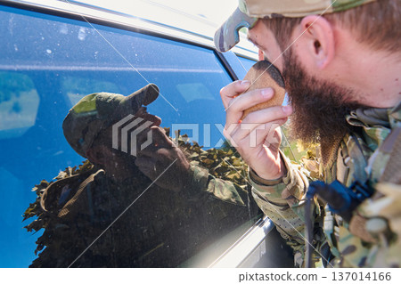 Soldier Applying Camouflage Face Paint With Sponge While Checking Reflection In Vehicle Window Soldier Applying Camouflage Face Paint With Sponge While Checking Reflection In Vehicle Window 137014166