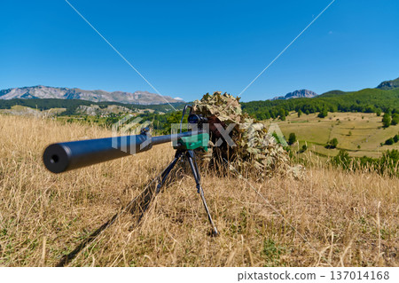 Sniper In Ghillie Suit Aiming A Rifle With Suppressor In Open Grassland Landscape 137014168