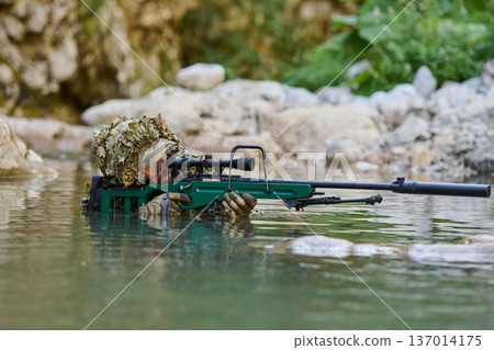 Military Sniper in Water With Suppressed Sniper Rifle Wearing Ghillie Camouflage and Tactical Gear 137014175