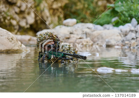 Sniper Soldier In Ghillie Suit Camouflaged In Water Aiming Rifle From Shallow River 137014189