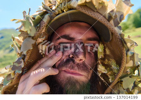 Camouflaged Soldier With Face Paint Applying Camouflage Makeup In Outdoor Training Closeup 137014199