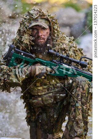 Camouflaged Sniper In Ghillie Suit Holding Scoped Rifle Kneeling In Water With Splashing Mud Camouflaged Sniper In Ghillie Suit Holding Scoped Rifle Kneeling In Water With Splashing Mud 137014225