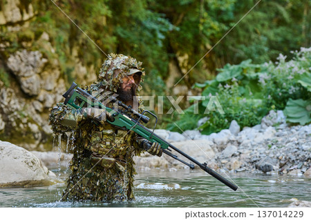 Sniper In Ghillie Suit Wading Through River With Camouflaged Sniper Rifle In Forest Ambush Sniper In Ghillie Suit Wading Through River With Camouflaged Sniper Rifle In Forest Ambush 137014229