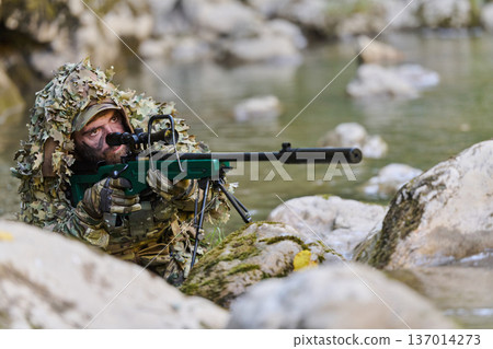 Camouflaged Sniper Soldier in Ghillie Suit Aiming Rifle From Riverbank Rocks Camouflaged Sniper Soldier in Ghillie Suit Aiming Rifle From Riverbank Rocks 137014273