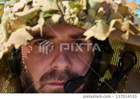 Close-Up Portrait Of A Focused Soldier Wearing Camouflage Ghillie Hood And Tactical Headset 137014310