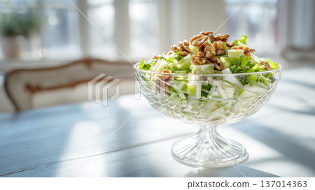 Elegant Close-Up of a Crisp Green Salad Topped with Celery Slices and Whole Walnuts, Served in a Crystal Pedestal Bowl on a Bright White Table 137014363