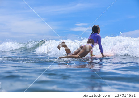 Woman Sitting On Surfboard Amid Breaking Wave Playful Beach Session 137014651