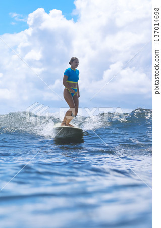Contented Woman Surfing On Her Longboard Under Golden Sunlight In Ocean 137014698