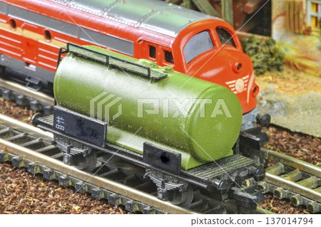 Detailed model of a green tank car with a red locomotive on a miniature railway track. A close-up view showcases a meticulously crafted green tank wagon alongside a vibrant red model train engine, set Detailed model of a green tank car with a red locomotive on a miniature railway track. A close-up view showcases a meticulously crafted green tank wagon alongside a vibrant red model train engine, set 137014794
