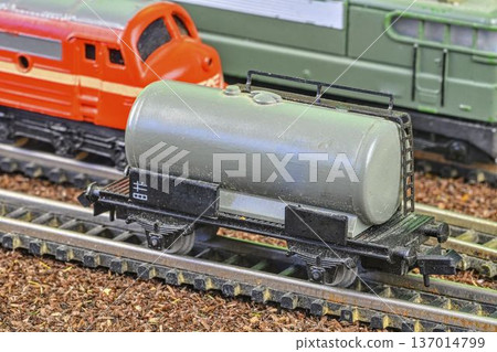 Close-up of a model train tank car on tracks with other trains in the background. Detailed view of a miniature gray tank car with intricate wheels and coupling, positioned on a model railway track Close-up of a model train tank car on tracks with other trains in the background. Detailed view of a miniature gray tank car with intricate wheels and coupling, positioned on a model railway track 137014799