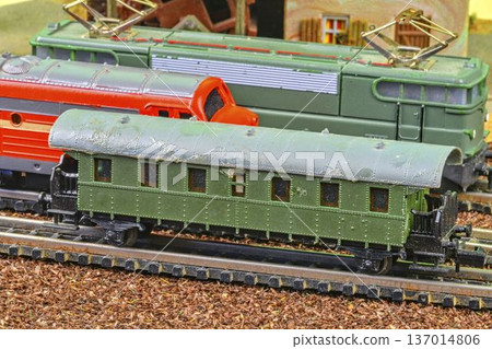 Close-up of vintage model train cars on a miniature railway track with detailed scenery. A detailed view of several model train cars, including a green passenger carriage and locomotives, arranged on Close-up of vintage model train cars on a miniature railway track with detailed scenery. A detailed view of several model train cars, including a green passenger carriage and locomotives, arranged on 137014806