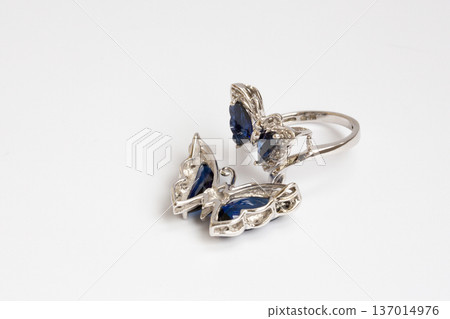 A women's piece of jewelry made of white gold, diamonds, and sapphires in the shape of a butterfly on a white background. A women's piece of jewelry made of white gold, diamonds, and sapphires in the shape of a butterfly on a white background. 137014976