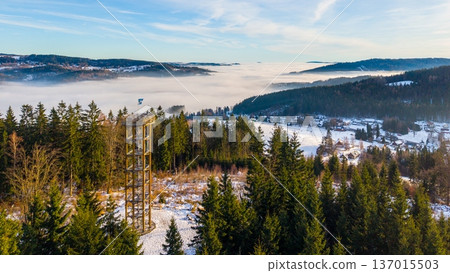 Svetly vrch lookout tower stands tall in Albrechtice, surrounded by snow-covered trees and hills. The view captures a foggy landscape below and the beauty of winter in the mountains. Svetly vrch lookout tower stands tall in Albrechtice, surrounded by snow-covered trees and hills. The view captures a foggy landscape below and the beauty of winter in the mountains. 137015503