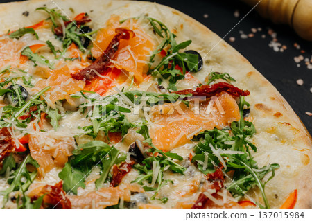 Gourmet pizza with salmon arugula cheese and sun dried tomatoes on wooden board Gourmet pizza with salmon arugula cheese and sun dried tomatoes on wooden board 137015984