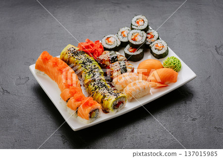 Assorted sushi rolls nigiri and sashimi served on white plate over dark background Assorted sushi rolls nigiri and sashimi served on white plate over dark background 137015985