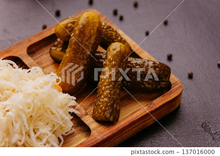 Pickled cucumbers with sauerkraut served on rustic wooden board over dark background 137016000