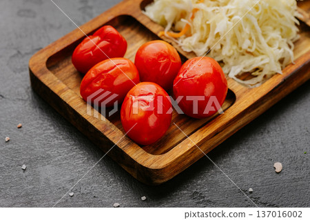 Pickled tomatoes and fermented cabbage served on rustic wooden board close up Pickled tomatoes and fermented cabbage served on rustic wooden board close up 137016002