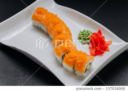 Salmon sushi roll with tobiko served with soy sauce chopsticks and wasabi on white plate 137016008