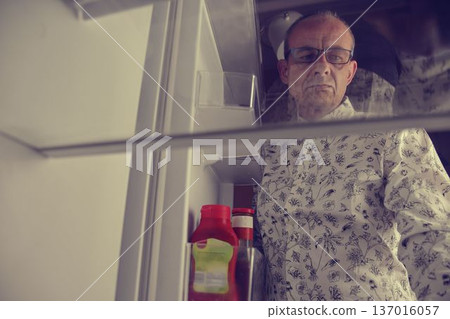 Hungry man looking for a late night meal in an empty fridge. Tired old man looking for a snack in the fridge at night, view from the fridge. Hungry man looking for a late night meal in an empty fridge 137016057