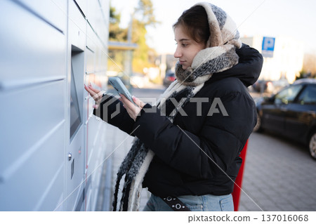 Young Girl Opens Outdoor Parcel Locker On A Street Using A Smartphone Young Girl Opens Outdoor Parcel Locker On A Street Using A Smartphone 137016068