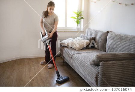 Young girl vacuums the floor in a living room during the day Young girl vacuums the floor in a living room during the day 137016074