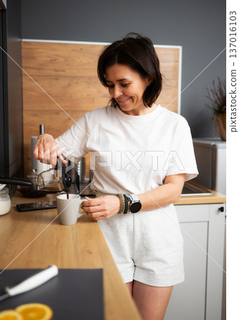 Smiling Girl Pours Fresh Coffee Into A Cup In The Kitchen In The Morning Smiling Girl Pours Fresh Coffee Into A Cup In The Kitchen In The Morning 137016103