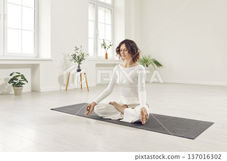 Peaceful sporty young woman doing yoga exercise sitting in lotus pose. 137016302