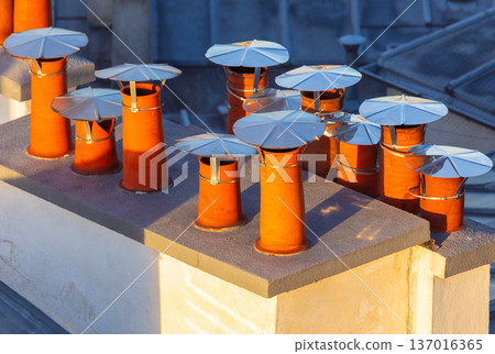 Clay rooftop chimneys with metal caps in warm morning light Clay rooftop chimneys with metal caps in warm morning light 137016365