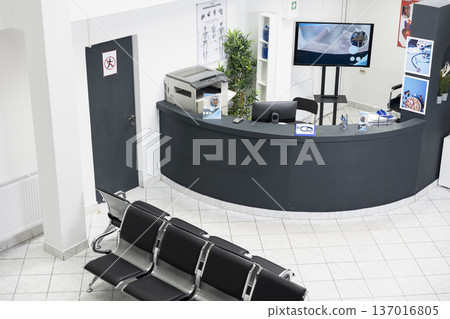 Unoccupied medical waiting area with modern furniture and computer at front desk, creating safe and sterile environment. Empty hospital lobby and healthcare office prepared for patients appointments. Unoccupied medical waiting area with modern furniture and computer at front desk, creating safe and sterile environment. Empty hospital lobby and healthcare office prepared for patients appointments. 137016805