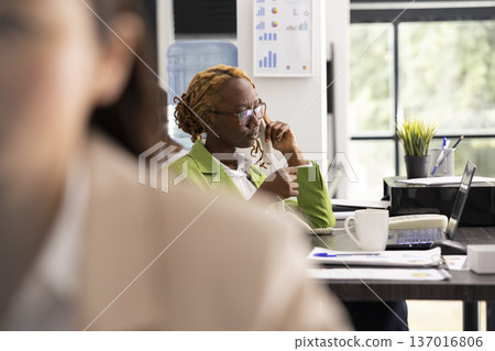 Black manager speaks on landline phone with internal employee, offering guidance and providing detailed work assessment. Businesswoman continues project brief and finalizes deal discussion with client Black manager speaks on landline phone with internal employee, offering guidance and providing detailed work assessment. Businesswoman continues project brief and finalizes deal discussion with client 137016806
