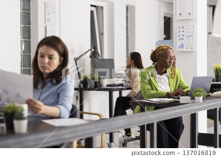 African american manager analyzing business emails and reviewing important information. Diverse professional women seated in office, working on daily tasks and contributing to company operations. African american manager analyzing business emails and reviewing important information. Diverse professional women seated in office, working on daily tasks and contributing to company operations. 137016819