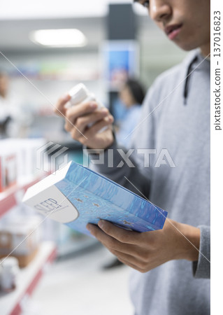 Close up of male customer comparing capsule and pill medications while carefully reading packaging information in pharmacy aisle. Man selects most suitable sleep aid at local dispensary. Close up of male customer comparing capsule and pill medications while carefully reading packaging information in pharmacy aisle. Man selects most suitable sleep aid at local dispensary. 137016823