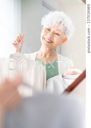 一位老婦人在鏡子前挑選衣服。 137016969
