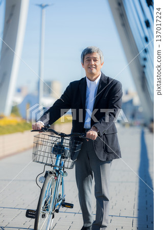 A man in his 60s walking while pushing a bicycle 137017224