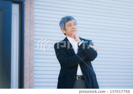 A man in his 60s thinking in front of the company building A man in his 60s thinking in front of the company building 137017788
