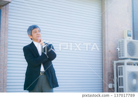 一位六十多歲的男子站在公司大樓前沉思。 一位六十多歲的男子站在公司大樓前沉思。 137017789
