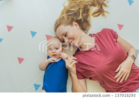 Mother and baby lying on a soft play mat at home, playing, talking and sharing a joyful moment together. Authentic family lifestyle, early childhood development and emotional bonding. Parenting and Mother and baby lying on a soft play mat at home, playing, talking and sharing a joyful moment together. Authentic family lifestyle, early childhood development and emotional bonding. Parenting and 137018293