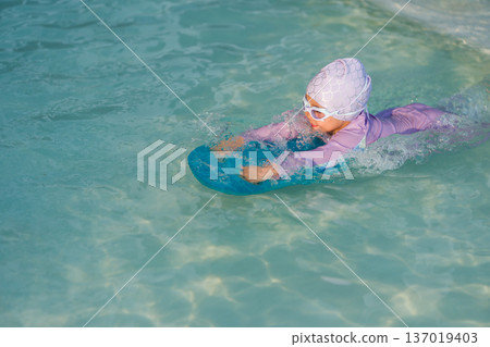 preschool child girl learning to swim with board in swimming pool preschool child girl learning to swim with board in swimming pool 137019403