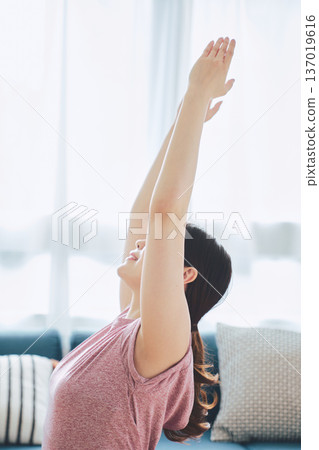 一位30多歲的女性在客廳做瑜伽,展現她的健身生活 一位30多歲的女性在客廳做瑜伽,展現她的健身生活 137019616