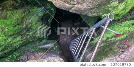 A metal ladder leading to the bottom of the cave. A narrow entrance to a stone cave in the mountains. High quality photo A metal ladder leading to the bottom of the cave. A narrow entrance to a stone cave in the mountains. High quality photo 137019780