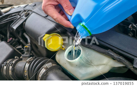 A man is pouring windshield washer fluid into the car's reservoir. Preparing for a road trip. High quality photo A man is pouring windshield washer fluid into the car's reservoir. Preparing for a road trip. High quality photo 137019855