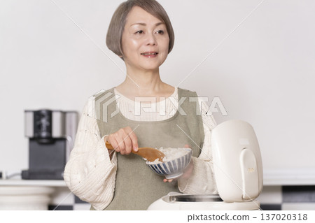 一位老婦人正在廚房裡把剛煮好的飯從電鍋裡倒進碗裡。 一位老婦人正在廚房裡把剛煮好的飯從電鍋裡倒進碗裡。 137020318