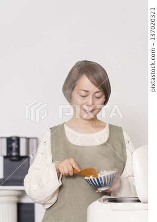 一位老婦人正在廚房裡把剛煮好的飯從電鍋裡倒進碗裡。 一位老婦人正在廚房裡把剛煮好的飯從電鍋裡倒進碗裡。 137020321