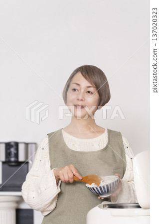 一位老婦人正在廚房裡把剛煮好的飯從電鍋裡倒進碗裡。 一位老婦人正在廚房裡把剛煮好的飯從電鍋裡倒進碗裡。 137020323