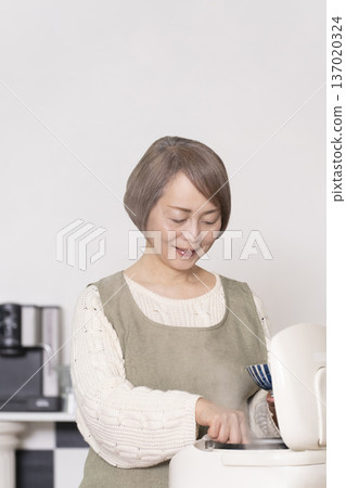 一位老婦人正在廚房裡把剛煮好的飯從電鍋裡倒進碗裡。 一位老婦人正在廚房裡把剛煮好的飯從電鍋裡倒進碗裡。 137020324