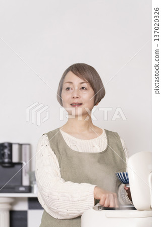 一位老婦人正在廚房裡把剛煮好的飯從電鍋裡倒進碗裡。 一位老婦人正在廚房裡把剛煮好的飯從電鍋裡倒進碗裡。 137020326