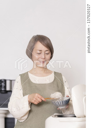 A senior woman pouring freshly cooked rice from a rice cooker into a bowl in the kitchen A senior woman pouring freshly cooked rice from a rice cooker into a bowl in the kitchen 137020327