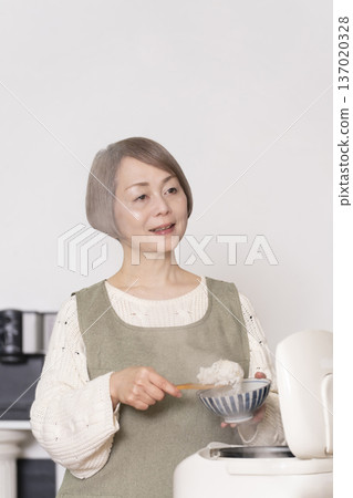 A senior woman pouring freshly cooked rice from a rice cooker into a bowl in the kitchen A senior woman pouring freshly cooked rice from a rice cooker into a bowl in the kitchen 137020328